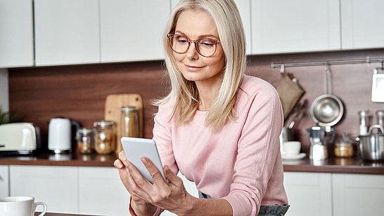 Eine ältere Dame mit Brille blickt auf ihr Smartphone